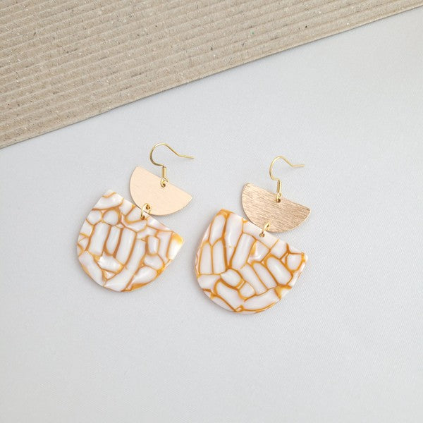 The Harper Pumpkin Spice Earrings make a bold statement with their gold-plated, geometric design elegantly displayed on a marble hexagonal platform.