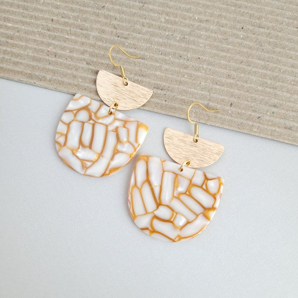 The Harper Pumpkin Spice Earrings make a bold statement with their gold-plated, geometric design elegantly displayed on a marble hexagonal platform.