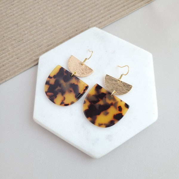 Harper Tortoise Earrings made of dangling tortoiseshell and 18K gold-plated finish are displayed on a hexagonal white marble surface, beautifully complementing the Harper Necklace.