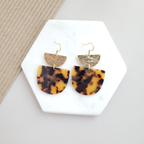 Harper Tortoise Earrings made of dangling tortoiseshell and 18K gold-plated finish are displayed on a hexagonal white marble surface, beautifully complementing the Harper Necklace.