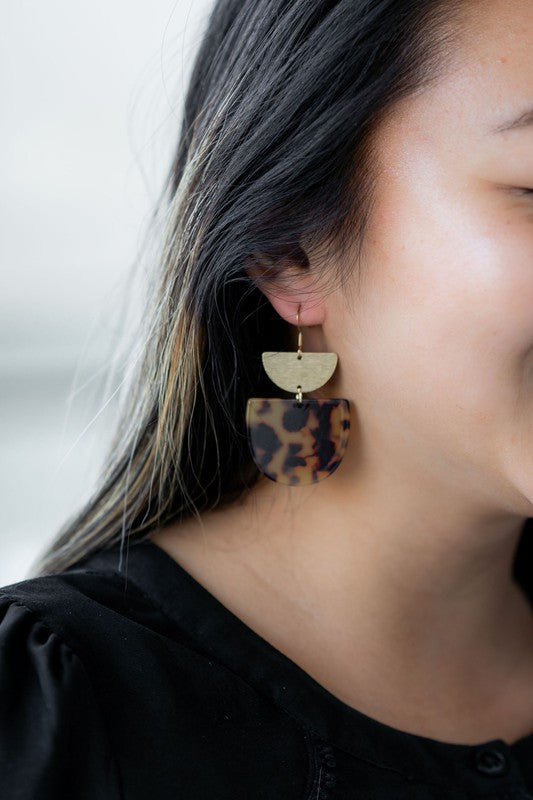 Harper Tortoise Earrings made of dangling tortoiseshell and 18K gold-plated finish are displayed on a hexagonal white marble surface, beautifully complementing the Harper Necklace.