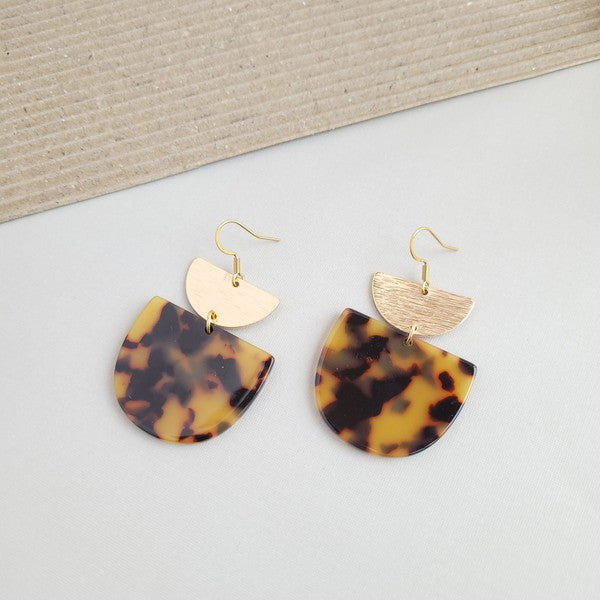 Harper Tortoise Earrings made of dangling tortoiseshell and 18K gold-plated finish are displayed on a hexagonal white marble surface, beautifully complementing the Harper Necklace.