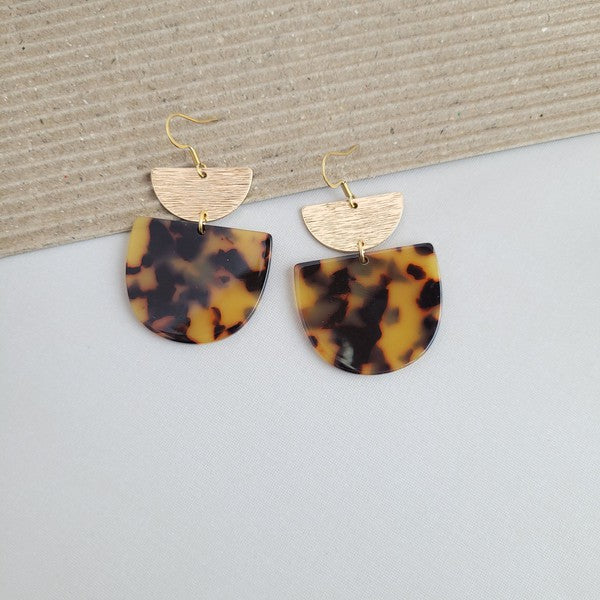 Harper Tortoise Earrings made of dangling tortoiseshell and 18K gold-plated finish are displayed on a hexagonal white marble surface, beautifully complementing the Harper Necklace.