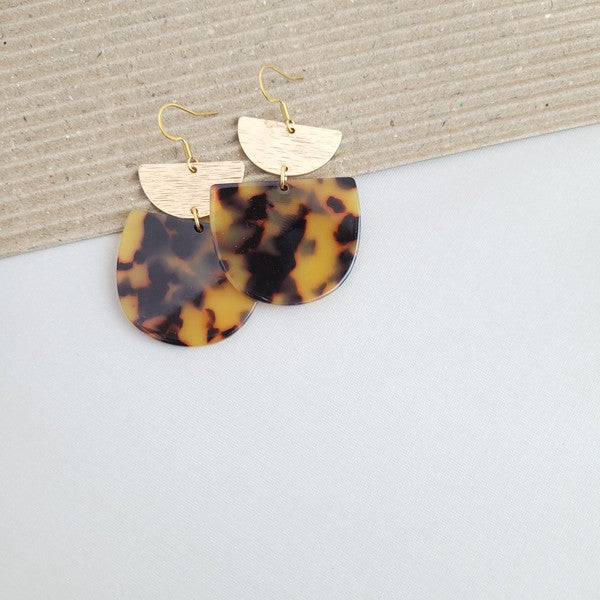 Harper Tortoise Earrings made of dangling tortoiseshell and 18K gold-plated finish are displayed on a hexagonal white marble surface, beautifully complementing the Harper Necklace.