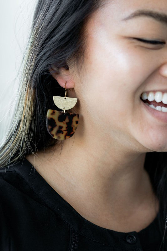 Harper Tortoise Earrings made of dangling tortoiseshell and 18K gold-plated finish are displayed on a hexagonal white marble surface, beautifully complementing the Harper Necklace.