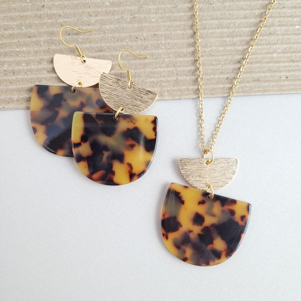 Harper Tortoise Earrings made of dangling tortoiseshell and 18K gold-plated finish are displayed on a hexagonal white marble surface, beautifully complementing the Harper Necklace.