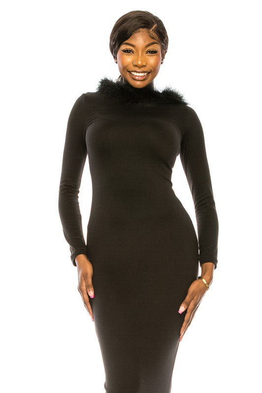 A woman in a black women's long dress with a hoodie and fur trim at the neckline is standing and smiling. She is wearing open-toe heels.