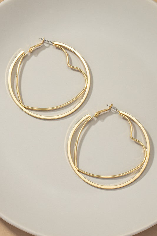 The heart hoop inside a circle hoop earrings, featuring shiny gold plating, are exquisitely presented on a light-colored plate.
