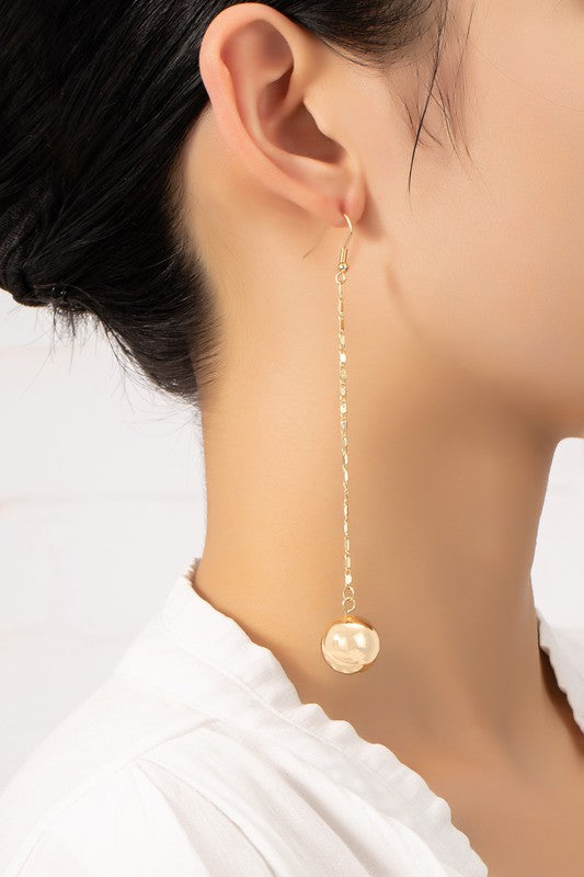 A woman, shown in profile, wears a white garment and the lightweight Long Chain with Dangling Ball Drop Earrings. The shiny gold plating and delicate design of her circular ornament earrings enhance her elegance.