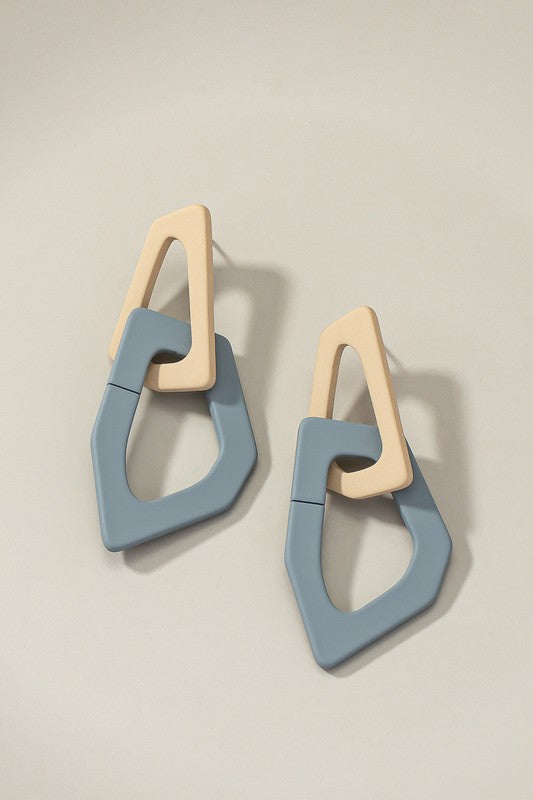 Close-up of lightweight acrylic earrings named "Organic Shape Chunky Link Drop Earrings," featuring interlocking triangular shapes in beige and gray, displayed on a flat surface.