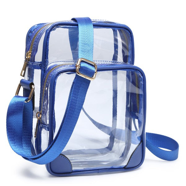 The See Thru Multi Compartment Crossbody Bag is a clear, rectangular transparent bag with blue trim and strap. This faux leather bag features two compartments with gold zippers and an adjustable shoulder strap.