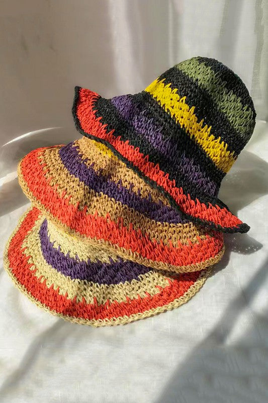 Three vibrant Packable crochet straw bucket hats with multi-color stripes are stacked elegantly on a plain background.