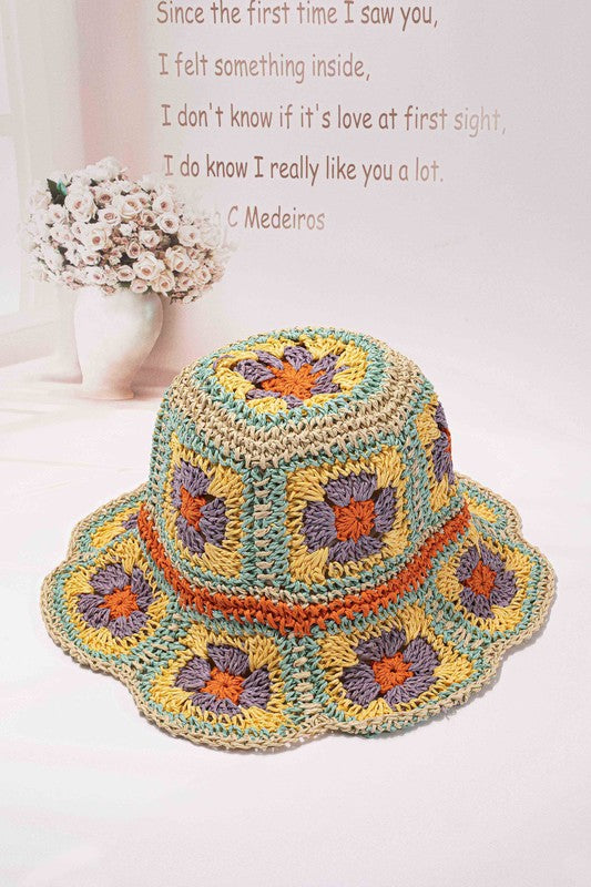 This packable crochet granny square bucket hat showcases exquisite hand-crocheted craftsmanship with a colorful pattern in shades of yellow, orange, and purple on a light background.