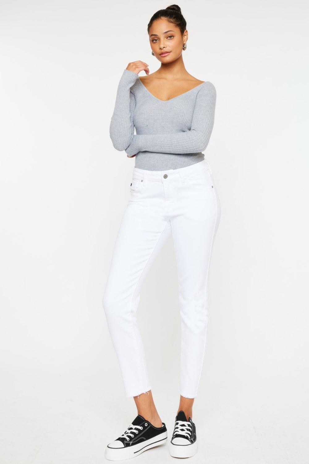 A person models a versatile gray long-sleeve top paired with flattering fit Kancan Mid Rise Ankle Skinny Jeans and sleek black sneakers, all set against a pristine white background.