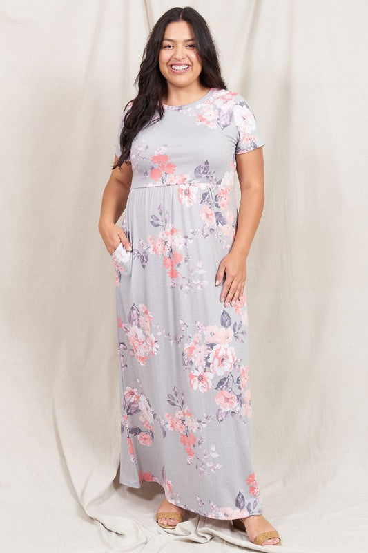 Against a neutral draped background, a woman stands smiling in the Vintage Floral Maxi Dress With Pockets, showcasing its short sleeves and practical design. This stylish gray ensemble, made in the United States, elegantly blends comfort with vintage charm.