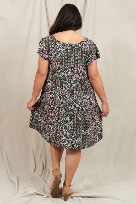 A person is standing and smiling, wearing the Plus Floral Flutter Sleeve Tunic, made from 100% polyester and holding a small wooden handbag. They are positioned against a neutral backdrop.