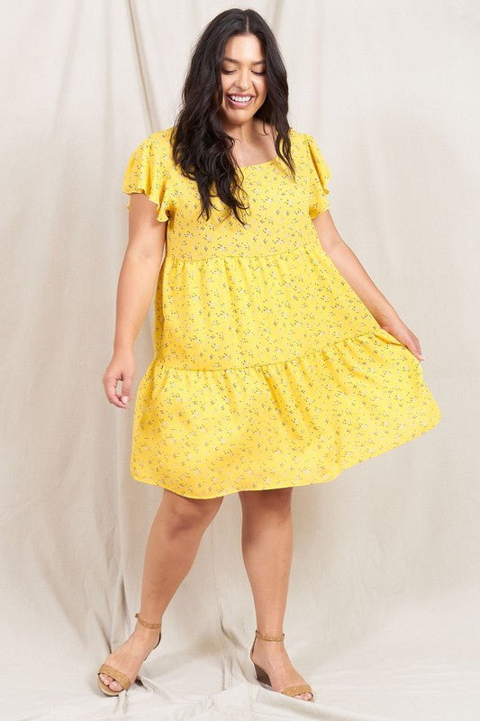 A person is standing and smiling, wearing the Plus Floral Flutter Sleeve Tunic, made from 100% polyester and holding a small wooden handbag. They are positioned against a neutral backdrop.