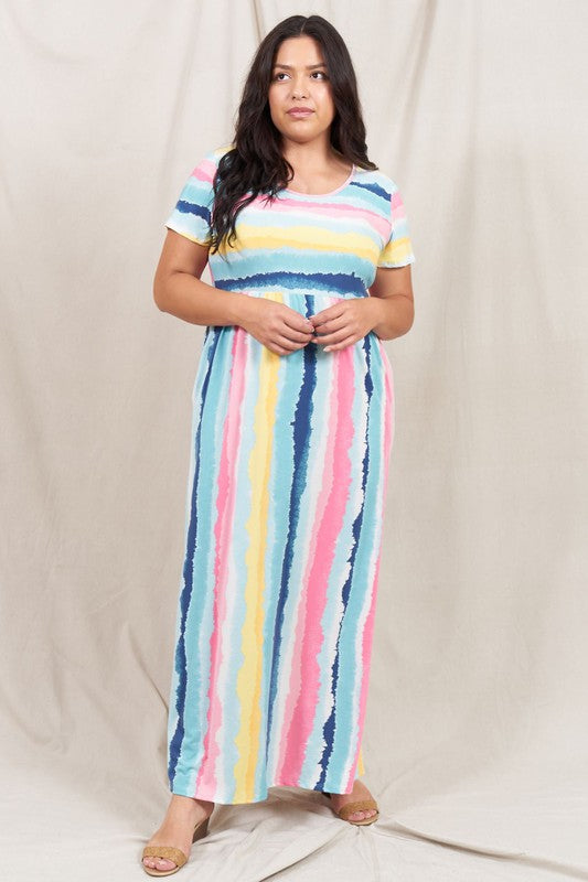 A woman stands against a beige backdrop, wearing the vibrant Water Color Short Sleeve Maxi Dress and holding a woven handbag. She has one hand in her dress pocket and is smiling.