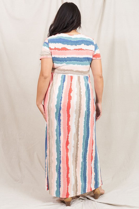 A woman stands against a beige backdrop, wearing the vibrant Water Color Short Sleeve Maxi Dress and holding a woven handbag. She has one hand in her dress pocket and is smiling.