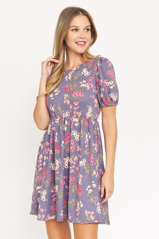 Woman wearing a Gathered Puff Sleeve Mini Dress in blue floral, made with a Polyester Spandex blend, standing against a plain white background.