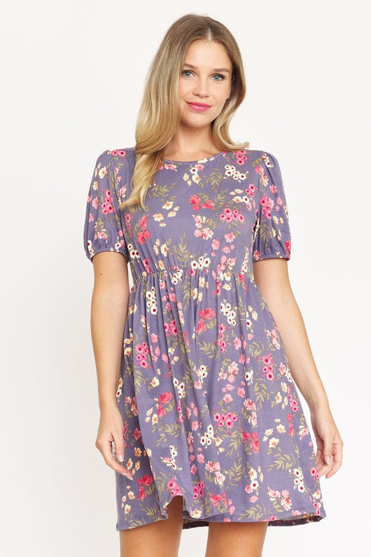 Woman wearing a Gathered Puff Sleeve Mini Dress in blue floral, made with a Polyester Spandex blend, standing against a plain white background.