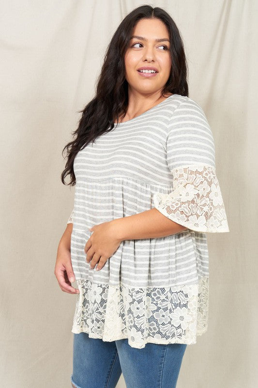 A woman wearing a Plus Lace Trim Tiered Tunic with striped design and lace details on the sleeves and hem stands in front of a plain beige background. She is also wearing ripped jeans.