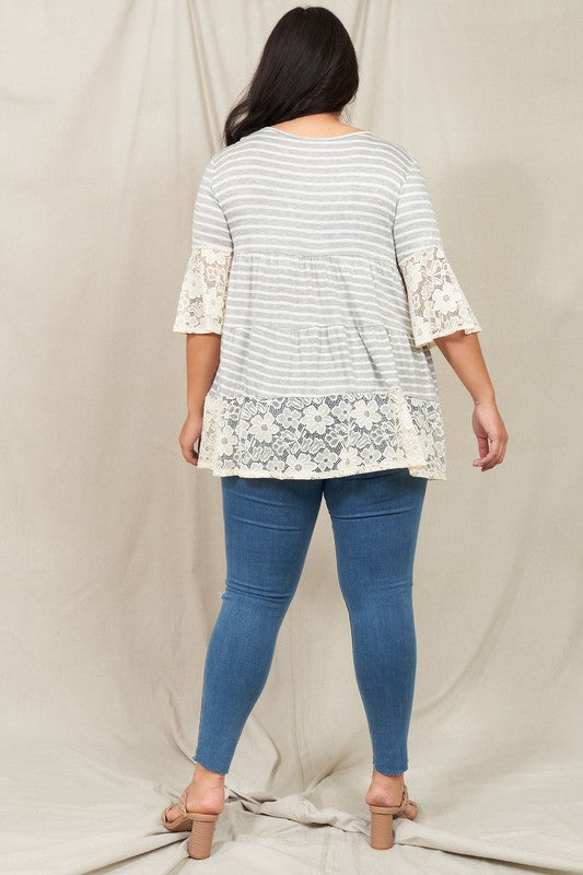 A woman wearing a Plus Lace Trim Tiered Tunic with striped design and lace details on the sleeves and hem stands in front of a plain beige background. She is also wearing ripped jeans.