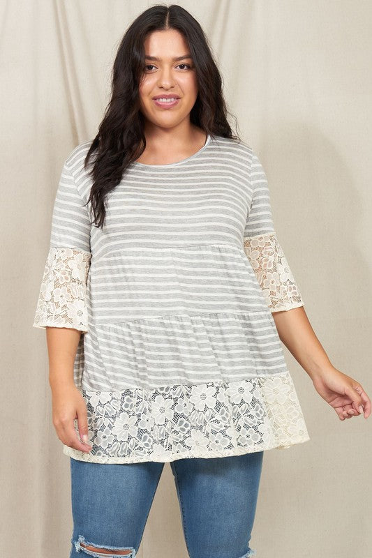 A woman wearing a Plus Lace Trim Tiered Tunic with striped design and lace details on the sleeves and hem stands in front of a plain beige background. She is also wearing ripped jeans.