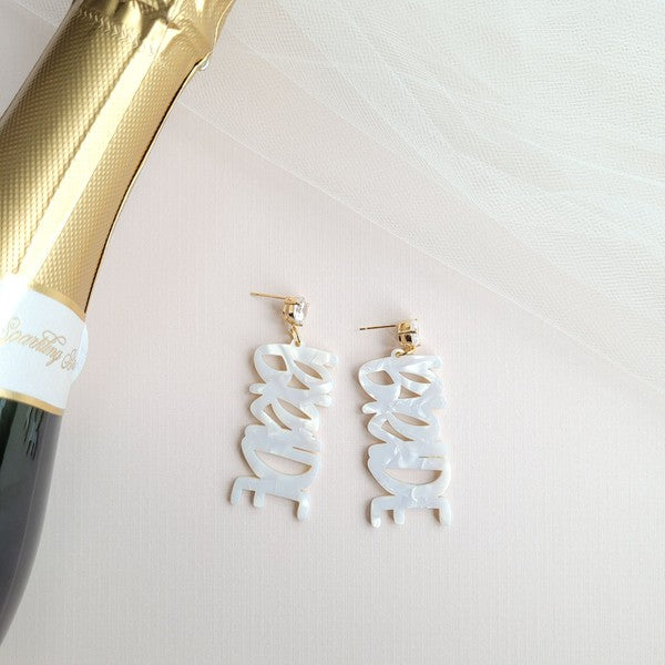 Bride earrings paired with a gold-capped champagne bottle, featuring elegant white script, ideal for a bridal shower and beautifully placed on a white fabric background.