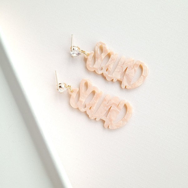 Two dangling earrings featuring "chaos" in peach-colored material, with exquisite hand-lettered calligraphy, are attached to gold posts adorned with clear stone accents. Perfectly named the "Bachelorette Squad," these earrings make a stunning bridal party gift and rest elegantly on a white surface.