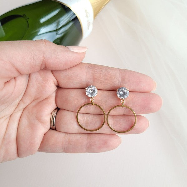 The I Do Earrings, adorned with gold and diamonds, rest elegantly on a hexagonal marble plate beside a champagne bottle, ready to catch the eye of wedding guests.