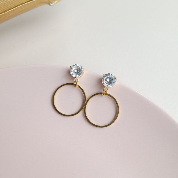 The I Do Earrings, adorned with gold and diamonds, rest elegantly on a hexagonal marble plate beside a champagne bottle, ready to catch the eye of wedding guests.