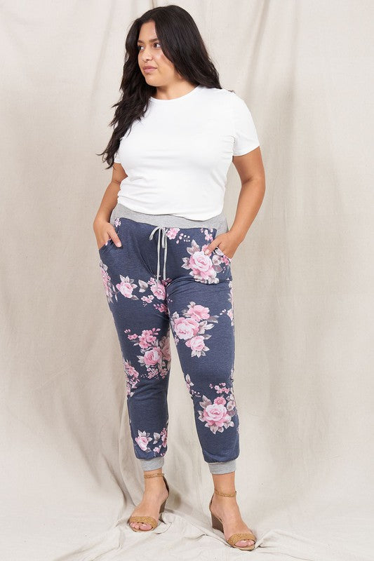 A woman stands smiling in the Plus Floral Drawstring Jogger and a white t-shirt, against a light beige background, showcasing American craftsmanship.