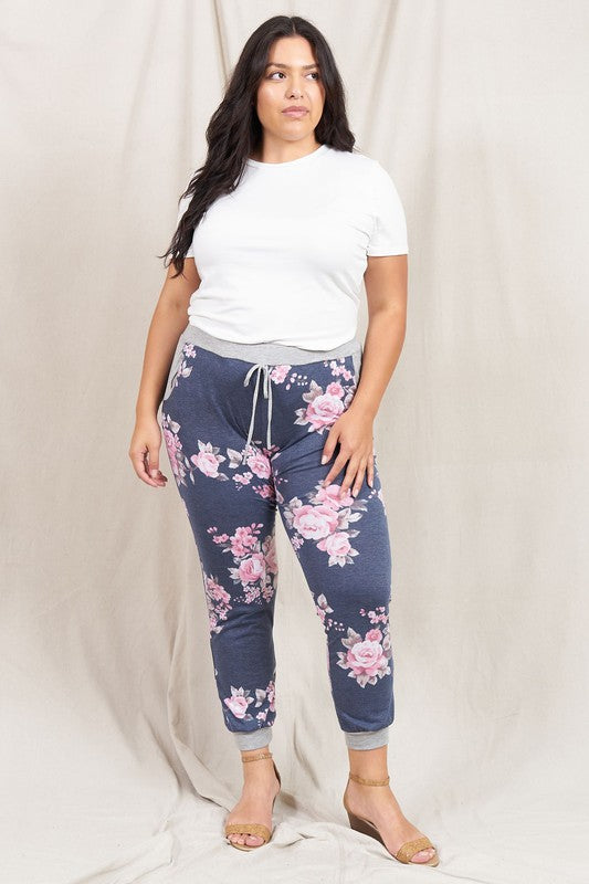 A woman stands smiling in the Plus Floral Drawstring Jogger and a white t-shirt, against a light beige background, showcasing American craftsmanship.