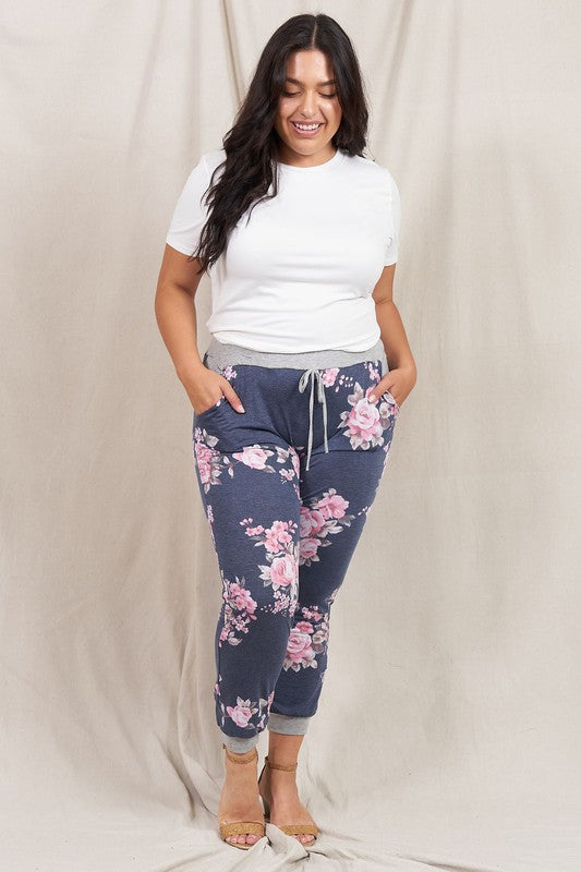 A woman stands smiling in the Plus Floral Drawstring Jogger and a white t-shirt, against a light beige background, showcasing American craftsmanship.