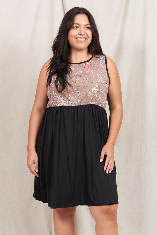 A woman in the Plus Sleeveless Branch Floral Midi Dress, showcasing a sheer polyester top and black skirt, stands gracefully before a beige curtain.