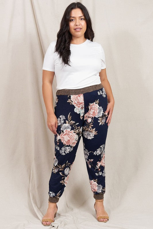 A person wearing a white t-shirt and the Plus Rose Print Jogger stands in front of a neutral backdrop, smiling slightly.