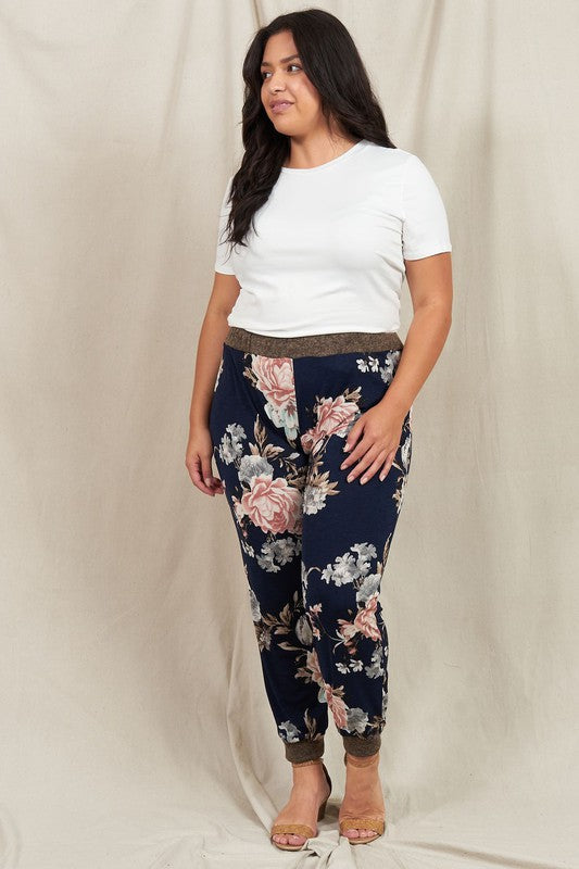 A person wearing a white t-shirt and the Plus Rose Print Jogger stands in front of a neutral backdrop, smiling slightly.