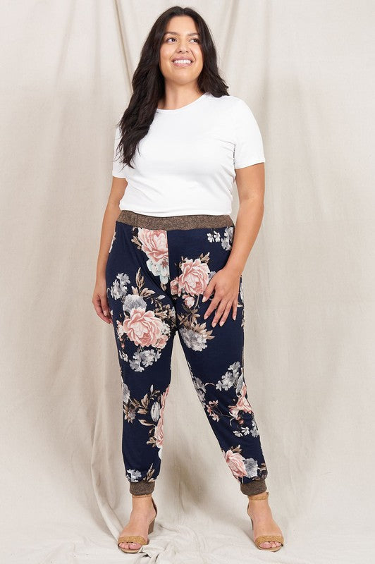 A person wearing a white t-shirt and the Plus Rose Print Jogger stands in front of a neutral backdrop, smiling slightly.