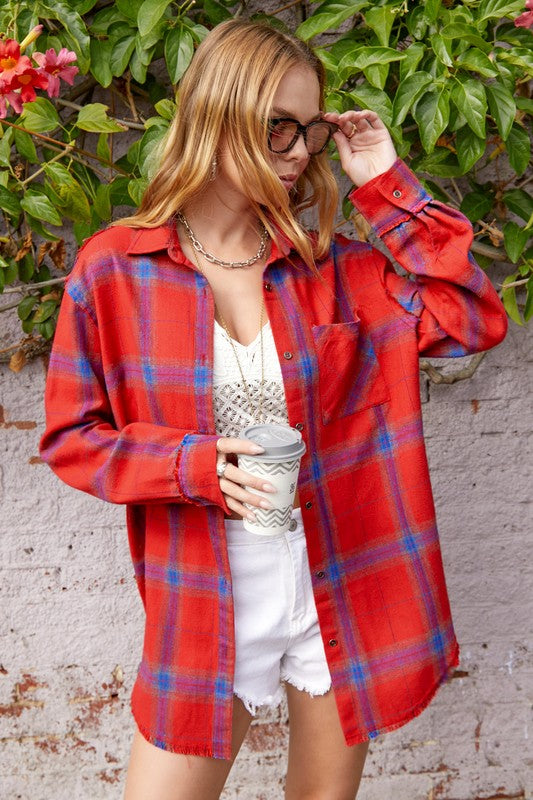 A person with long blonde hair wearing a black cap and an oversized Celine Shirt, which features a blue checkered plaid flannel design, showing a slight smile against a neutral background.