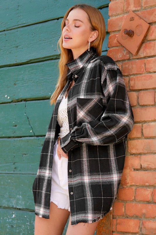 A person with long blonde hair wearing a black cap and an oversized Celine Shirt, which features a blue checkered plaid flannel design, showing a slight smile against a neutral background.