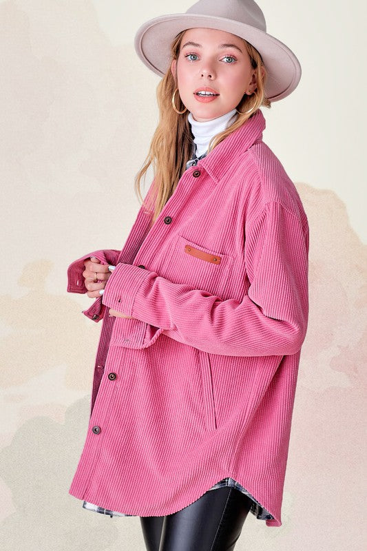 A person wearing a pink Chaser Madera Cozy Button Down Shacket, black pants, and a beige hat stands against a pastel-colored background, showcasing a casual chic look.