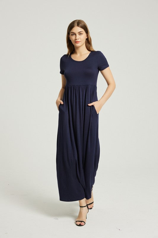 A woman strides confidently forward on a plain background, dressed in a navy blue Women's Summer Casual Maxi Dress with Pocket. This solid-patterned dress, designed with short sleeves and practical pockets, perfectly complements her graceful walk.