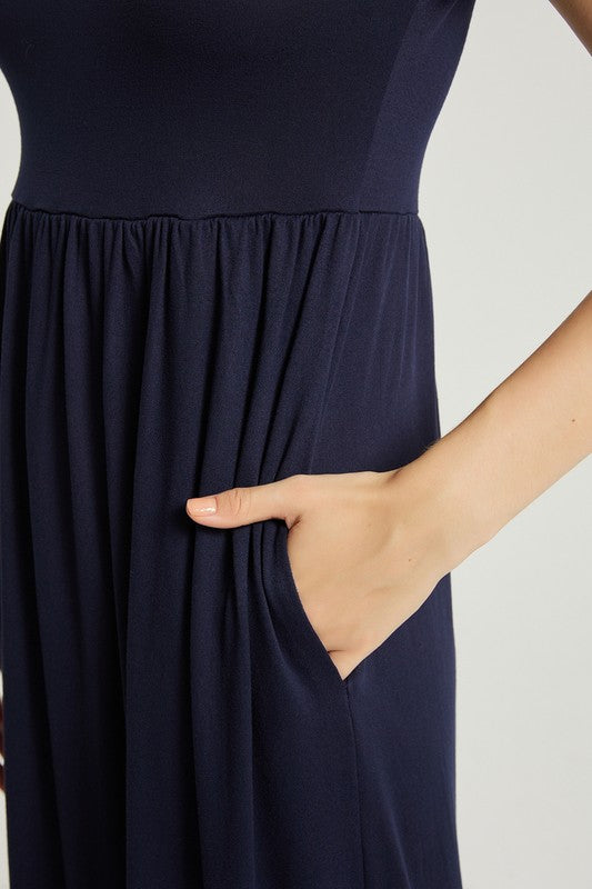 A woman strides confidently forward on a plain background, dressed in a navy blue Women's Summer Casual Maxi Dress with Pocket. This solid-patterned dress, designed with short sleeves and practical pockets, perfectly complements her graceful walk.