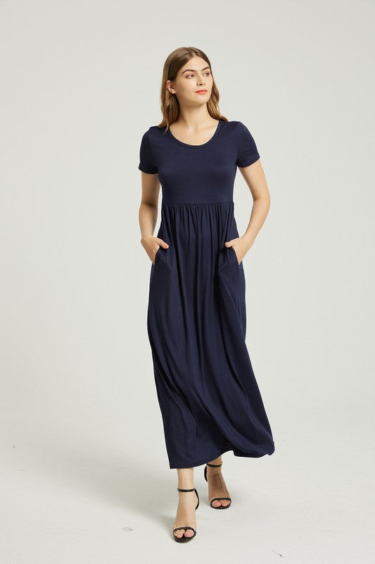 A woman strides confidently forward on a plain background, dressed in a navy blue Women's Summer Casual Maxi Dress with Pocket. This solid-patterned dress, designed with short sleeves and practical pockets, perfectly complements her graceful walk.