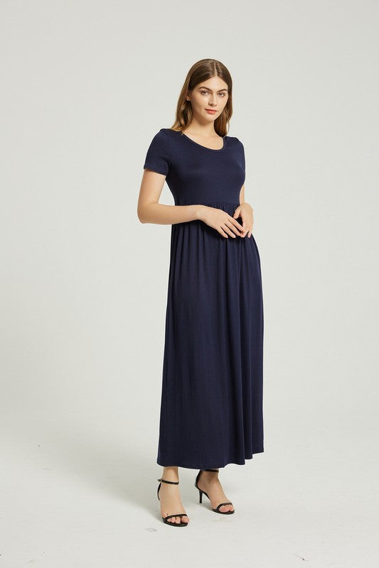 A woman strides confidently forward on a plain background, dressed in a navy blue Women's Summer Casual Maxi Dress with Pocket. This solid-patterned dress, designed with short sleeves and practical pockets, perfectly complements her graceful walk.