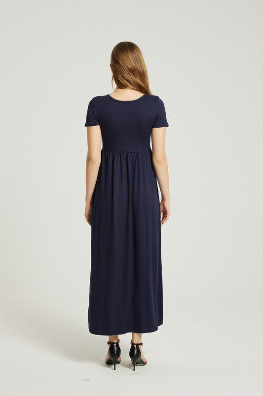 A woman strides confidently forward on a plain background, dressed in a navy blue Women's Summer Casual Maxi Dress with Pocket. This solid-patterned dress, designed with short sleeves and practical pockets, perfectly complements her graceful walk.