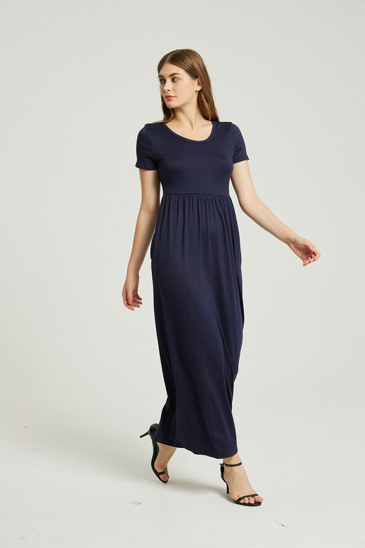 A woman strides confidently forward on a plain background, dressed in a navy blue Women's Summer Casual Maxi Dress with Pocket. This solid-patterned dress, designed with short sleeves and practical pockets, perfectly complements her graceful walk.