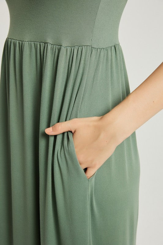 A woman wearing a Women's Summer Casual Maxi Dress With Pocket in green is seated on a white chair against a plain background.