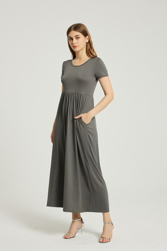 A woman in a grey Women's Summer Casual Maxi Dress With Pocket, featuring an A-line silhouette and chic pocket style, stands with her hands in her pockets against a plain background. She is wearing light-colored sandals.